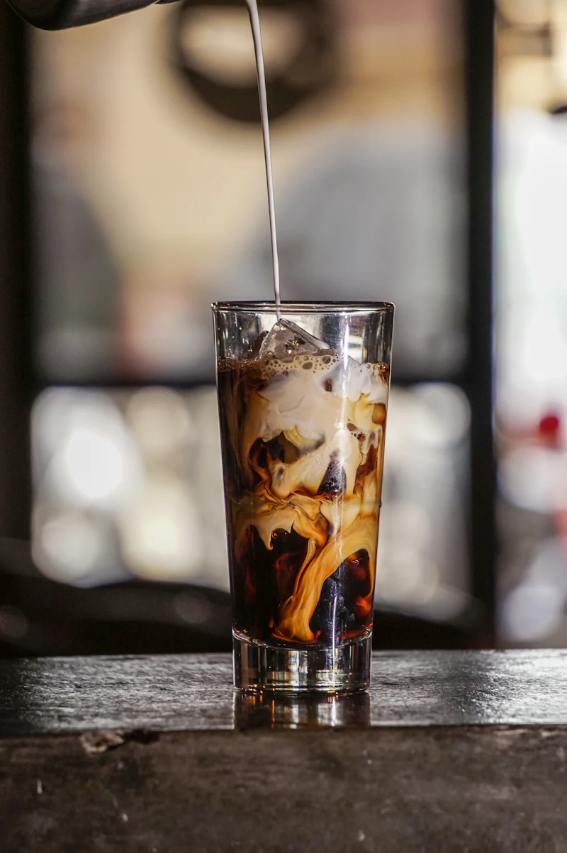 Cream poured into a tall glass of iced coffee